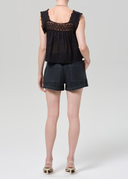 Person wearing a black sleeveless top with lace details and black shorts on a grey background
