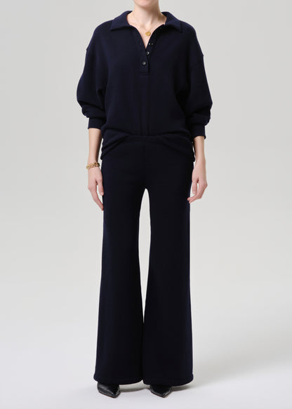 A model wearing a dark navy blue knit two-piece set consisting of a long-sleeve polo-style top and matching wide-leg trousers, photographed against a grey background.