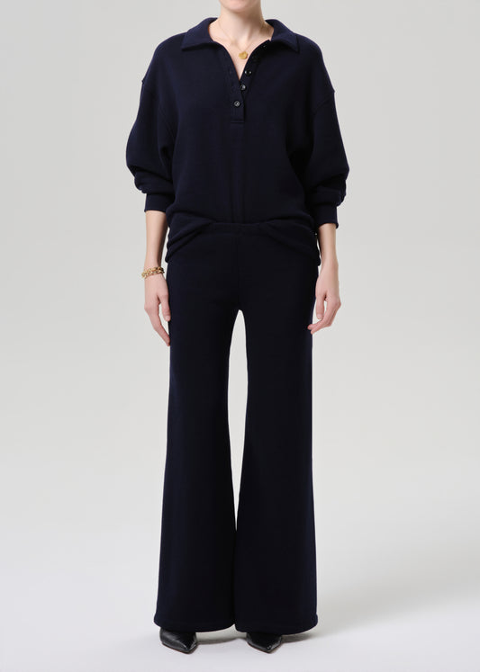A model wearing a dark navy blue knit two-piece set consisting of a long-sleeve polo-style top and matching wide-leg trousers, photographed against a grey background.