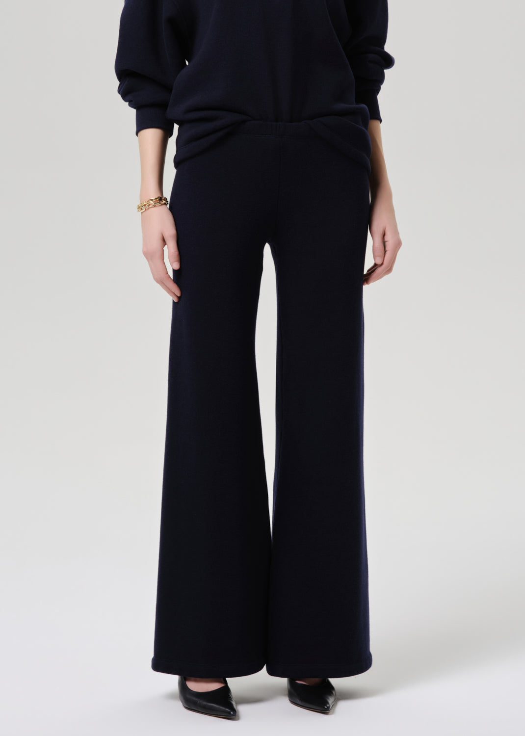Person wearing black wide-leg pants and a dark top on a grey background.