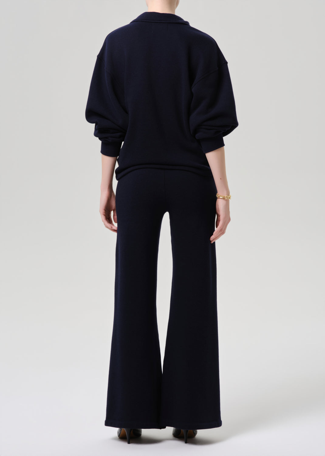 Person wearing a black outfit with wide-leg pants on a grey background.