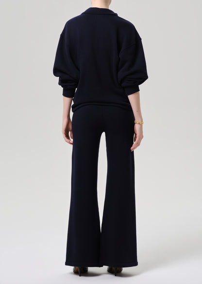 Person wearing a black outfit with wide-leg pants on a grey background.