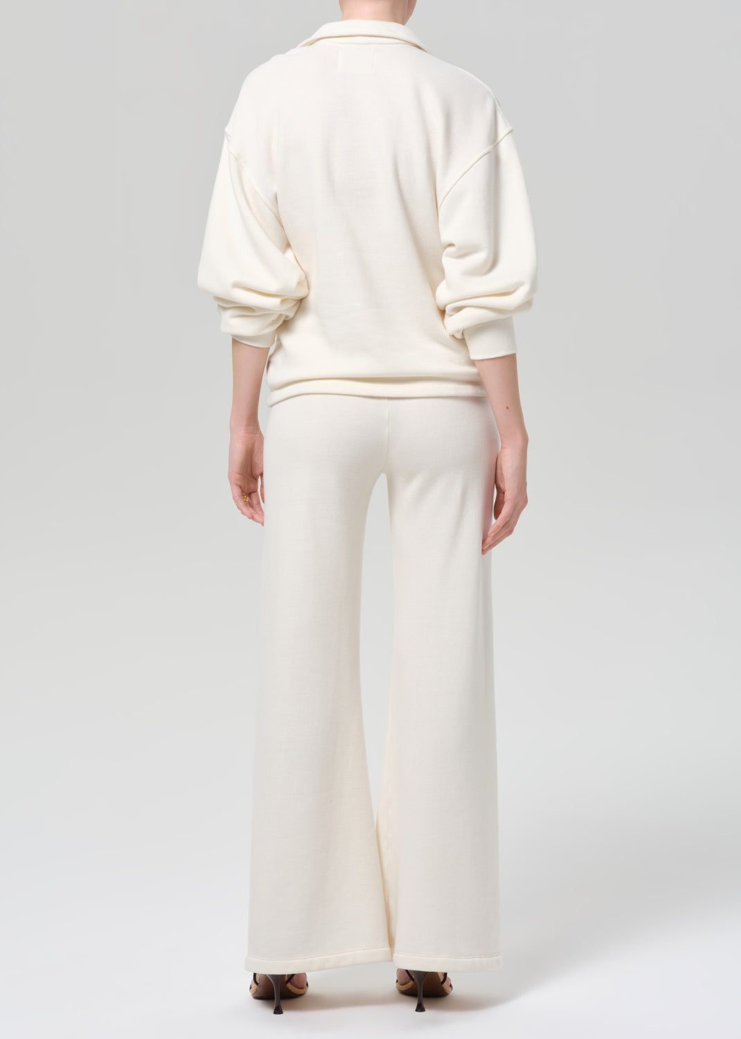 Person wearing a cream-colored sweatshirt and pants on a plain background