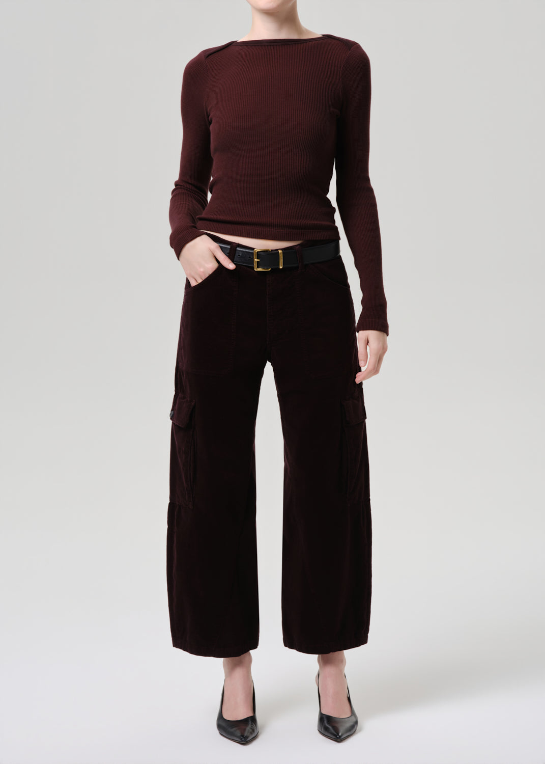 Person wearing a burgundy long-sleeve top and dark brown wide-leg pants on a grey background