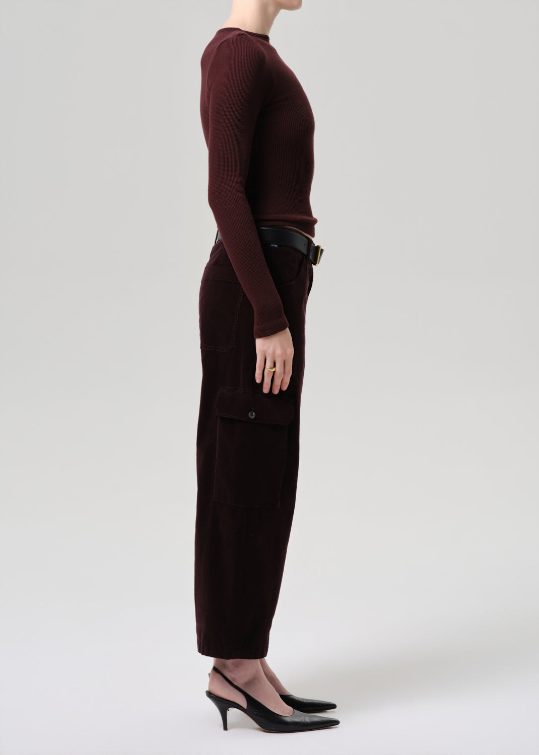 Person wearing a burgundy long-sleeve top and dark pants on a grey background