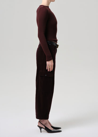 Person wearing a burgundy long-sleeve top and dark pants on a grey background