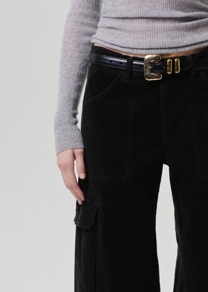 Person wearing dark green pants with a gold belt buckle on a grey background