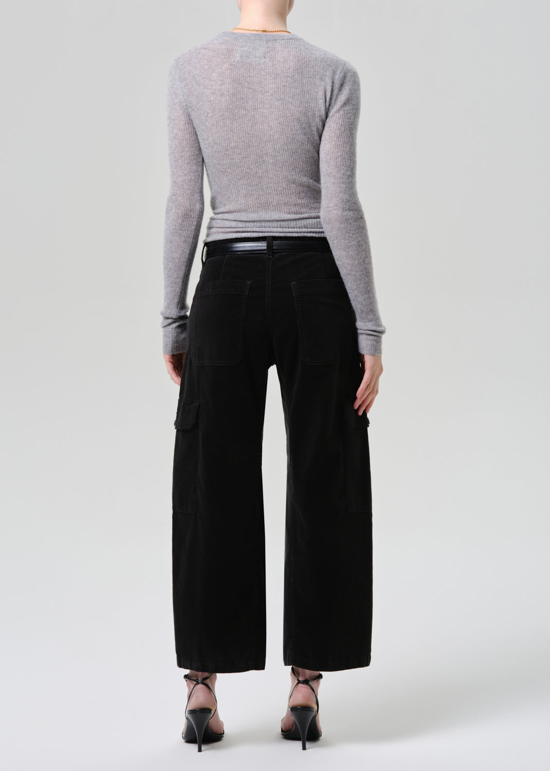 Person wearing a grey long-sleeve top and dark green wide-leg pants on a grey background