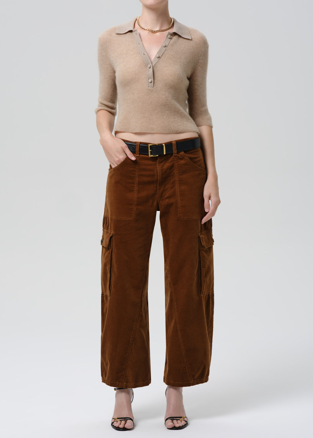 Person wearing a beige sweater and brown cargo pants on a grey background