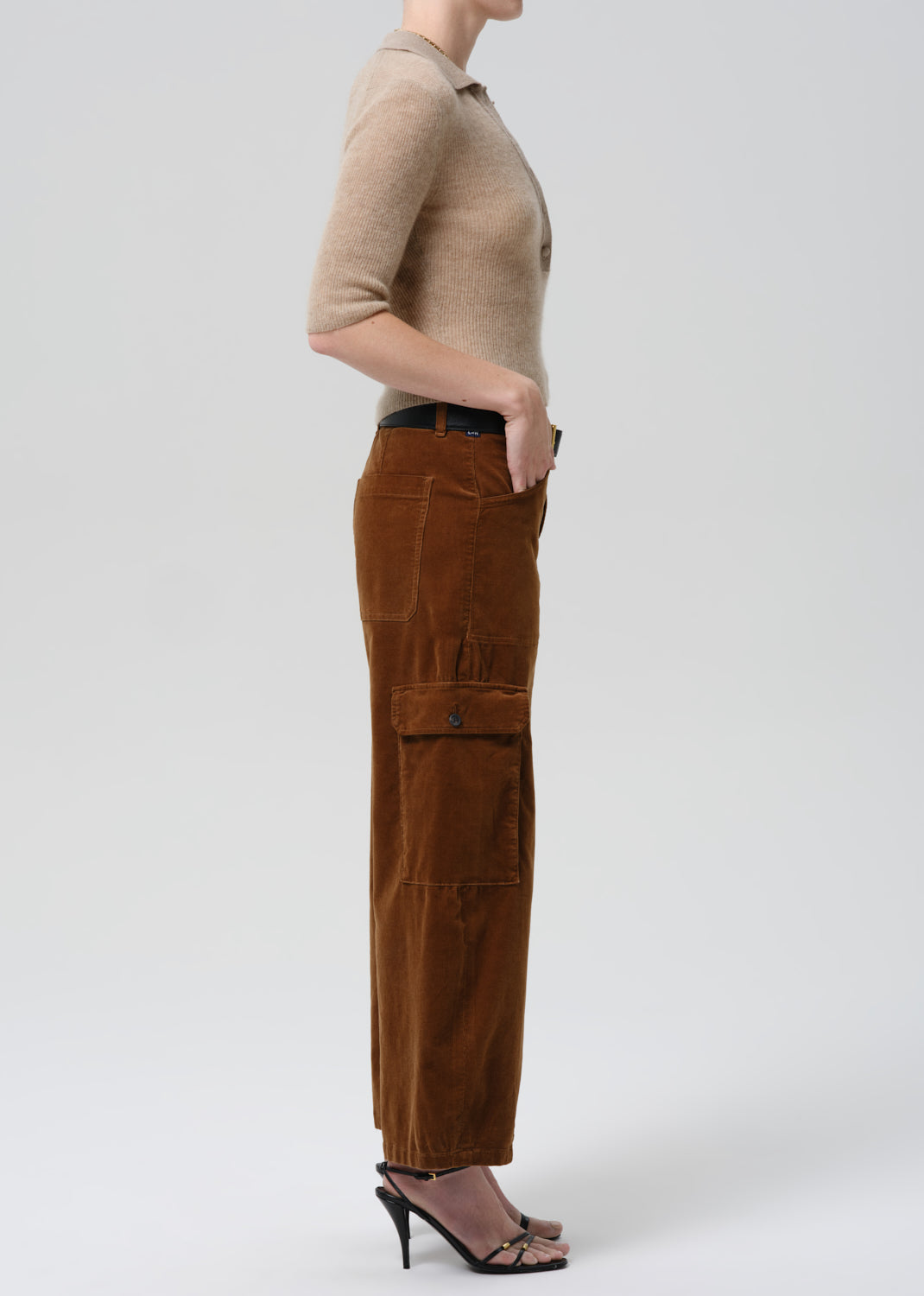 Person wearing a beige top and brown pants on a grey background