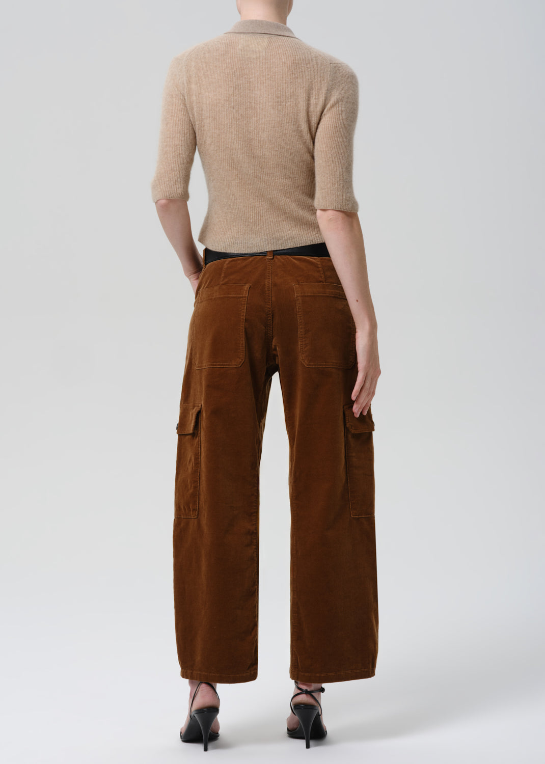 Person wearing a beige sweater and brown cargo pants on a grey background