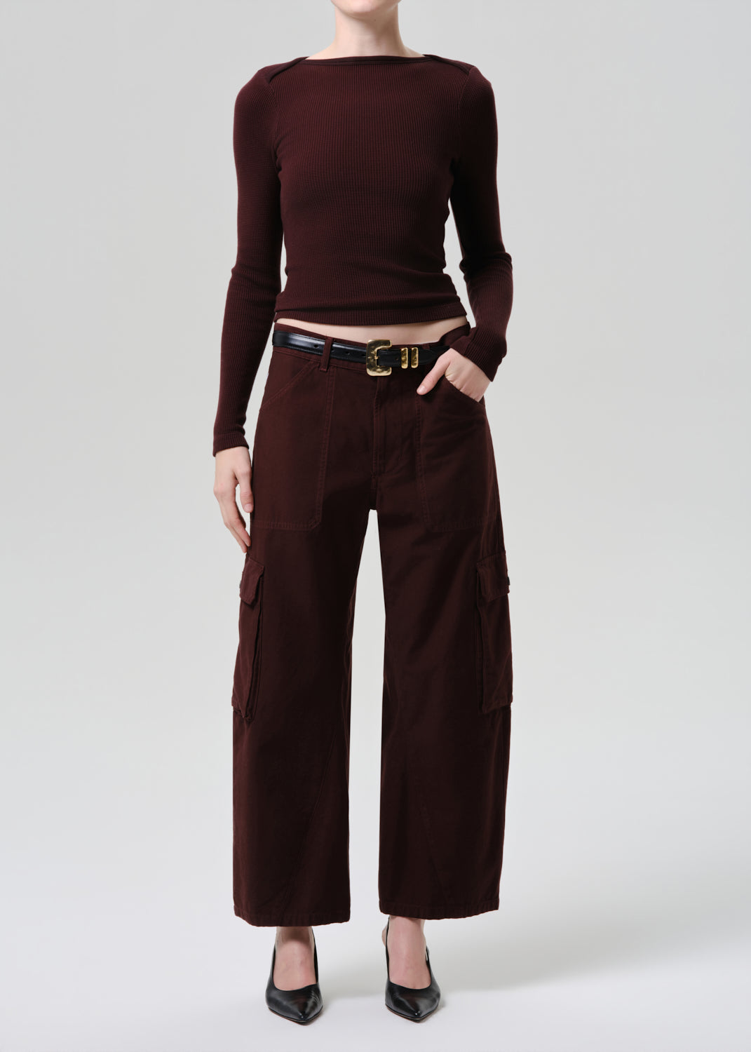 Person wearing a brown long-sleeve top and wide-leg pants on a grey background