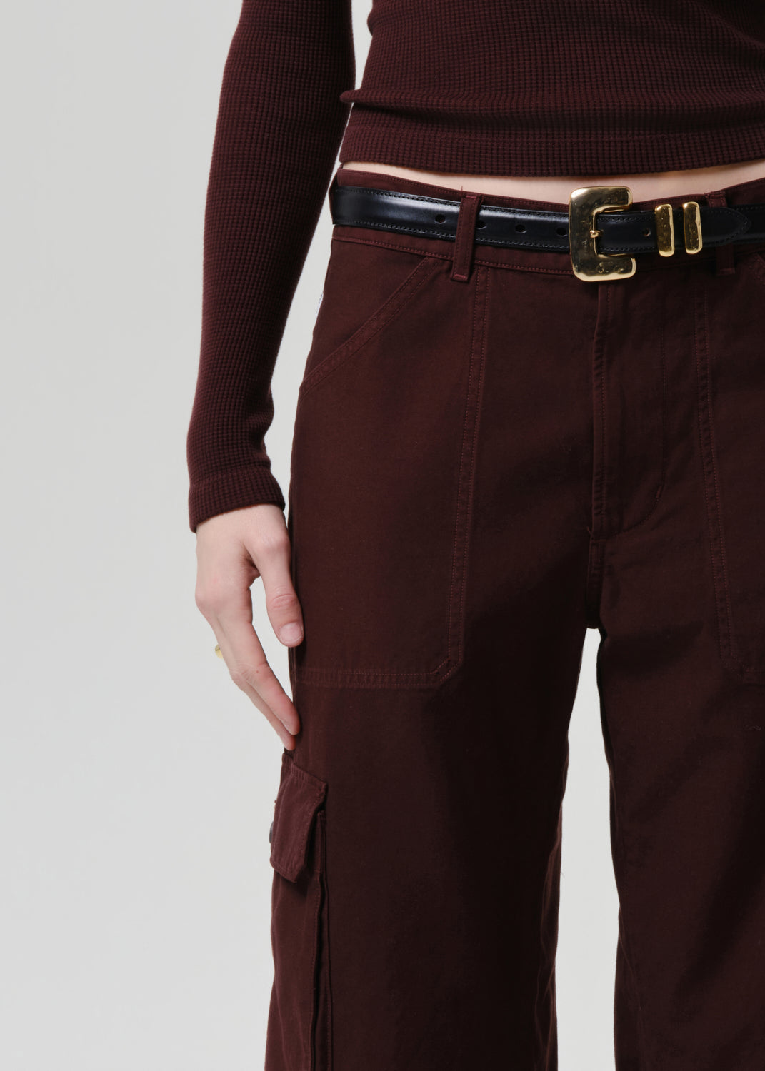 Person wearing a brown outfit with a belt on a grey background