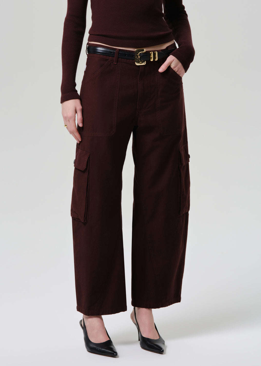 Person wearing brown cargo pants with a belt on a grey background