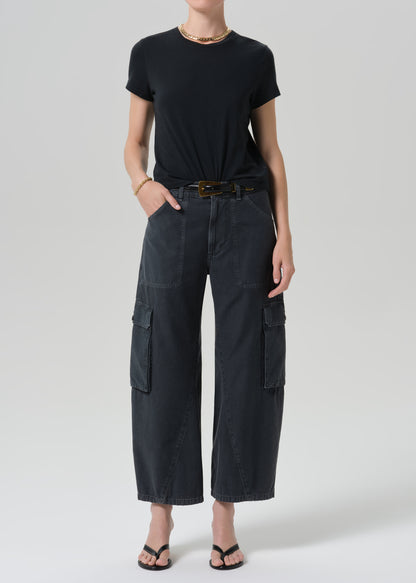 A model wearing a black short-sleeve t-shirt and dark charcoal gray wide-leg cargo pants with a black belt, styled with black sandals and a gold necklace against a grey background.