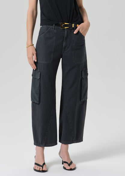 A model wearing black wide-leg cropped cargo pants with a black top, a gold-buckled belt, and black sandals, shown from the waist down against a grey background.