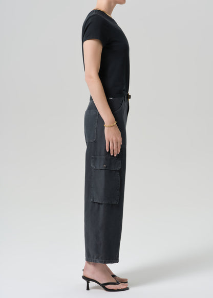 A model shown in profile wearing a black short-sleeve t-shirt and dark charcoal gray wide-leg cargo pants with flap pockets, paired with black heeled sandals, against a grey background.