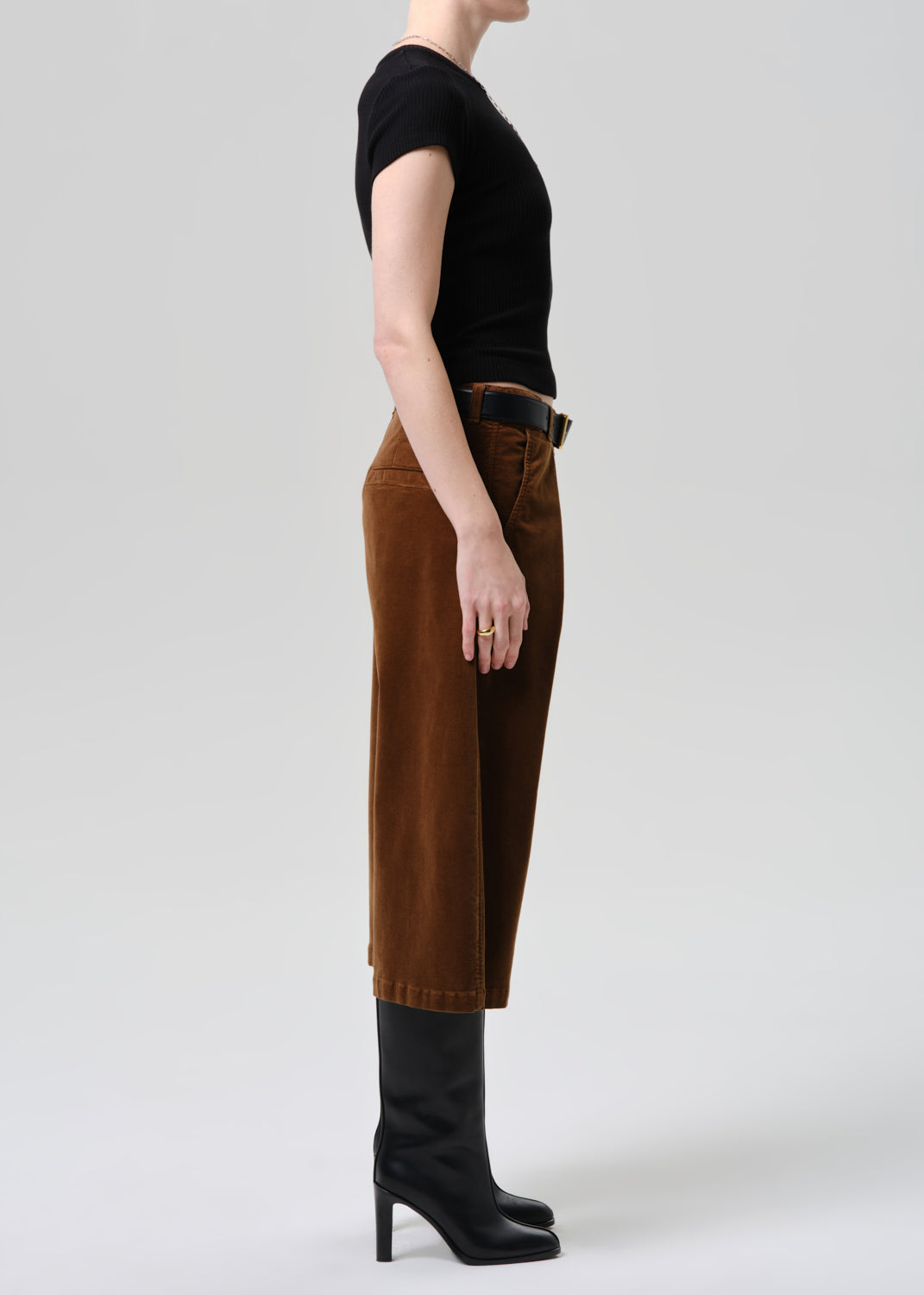 Person wearing brown pants and black boots on a grey background