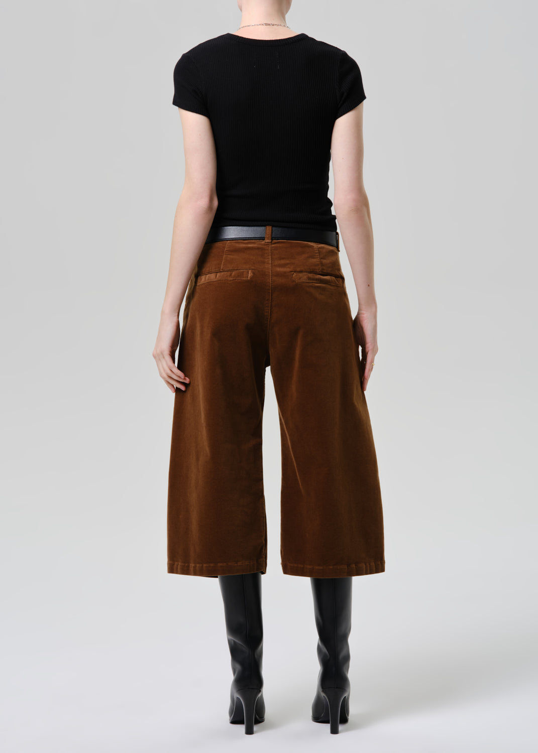 Person wearing brown wide-leg pants and black top on a grey background