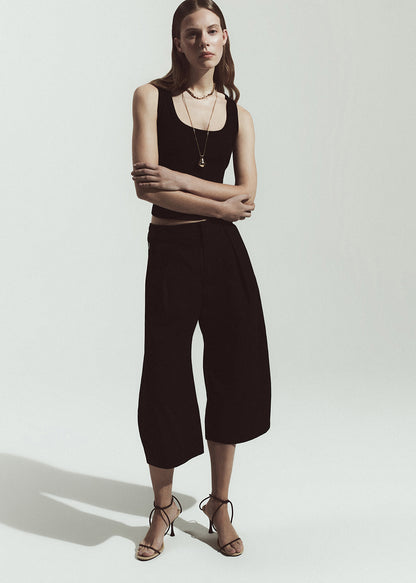 Person wearing a black outfit with wide-leg pants on a grey background