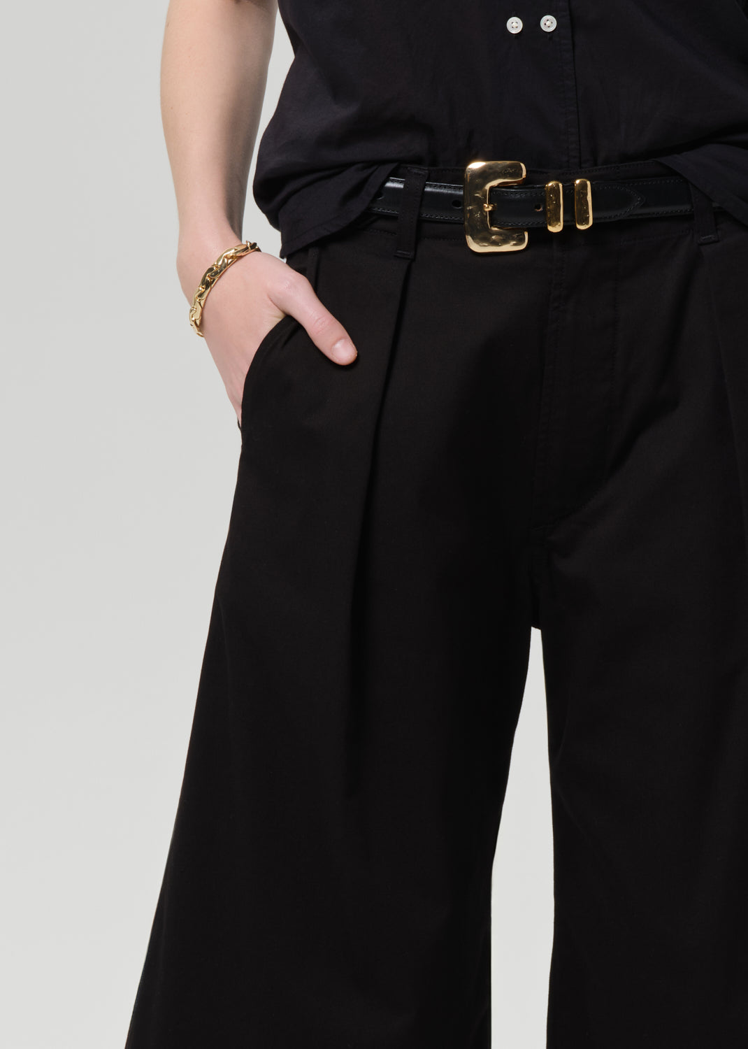 Person wearing a black outfit with wide-leg pants on a grey background