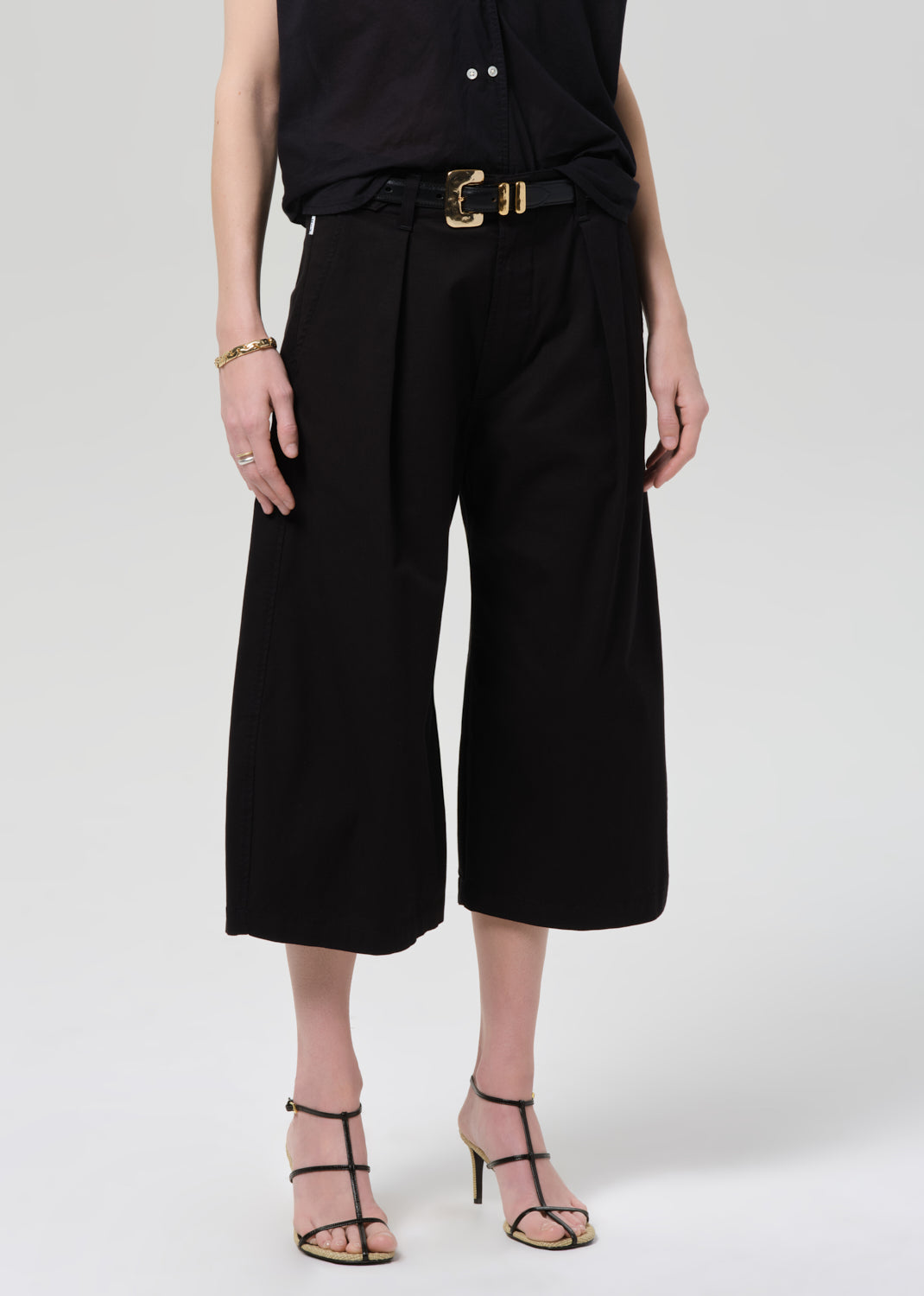 Person wearing a black outfit with wide-leg pants on a grey background