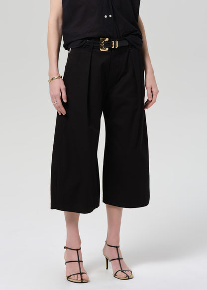 Person wearing a black outfit with wide-leg pants on a grey background