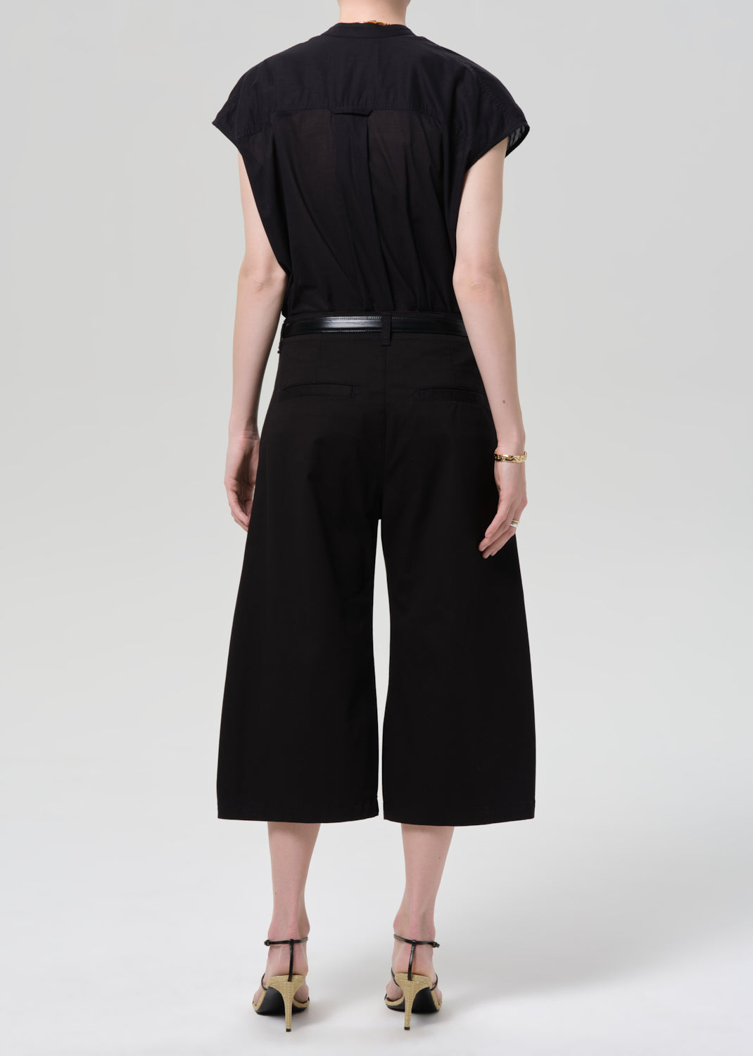 Person wearing a black outfit with wide-leg pants on a grey background