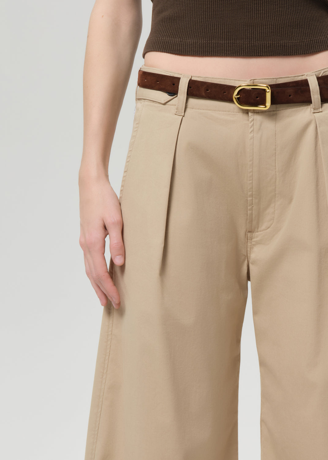 Person wearing a brown sleeveless top and beige wide-leg pants on a grey background