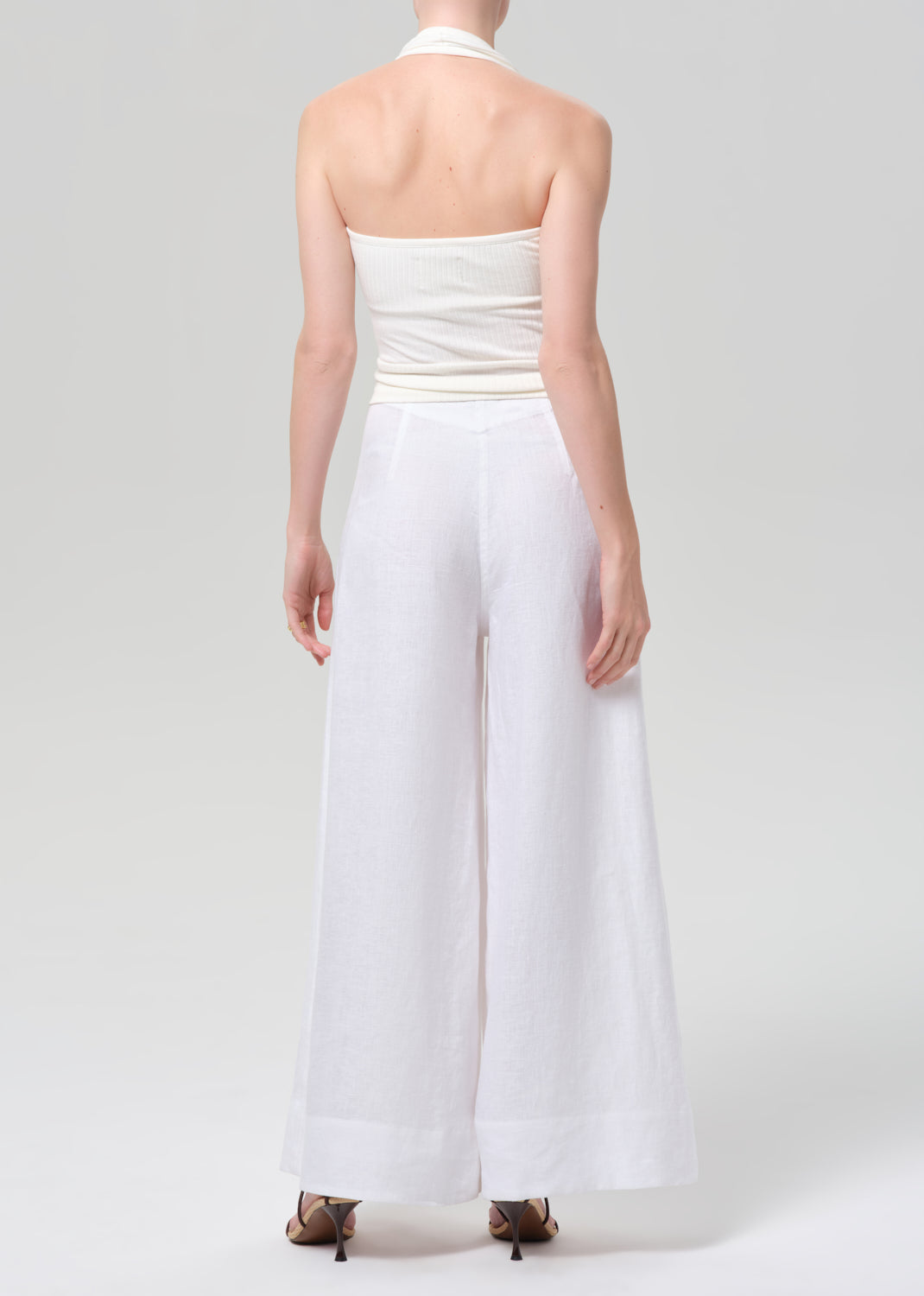 Woman wearing a white halter top and palazzo pants on a light gray background