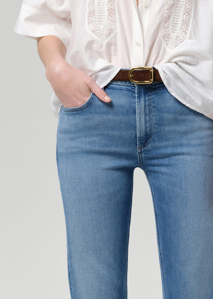Person wearing a white blouse and blue jeans with a gold belt on a light gray background