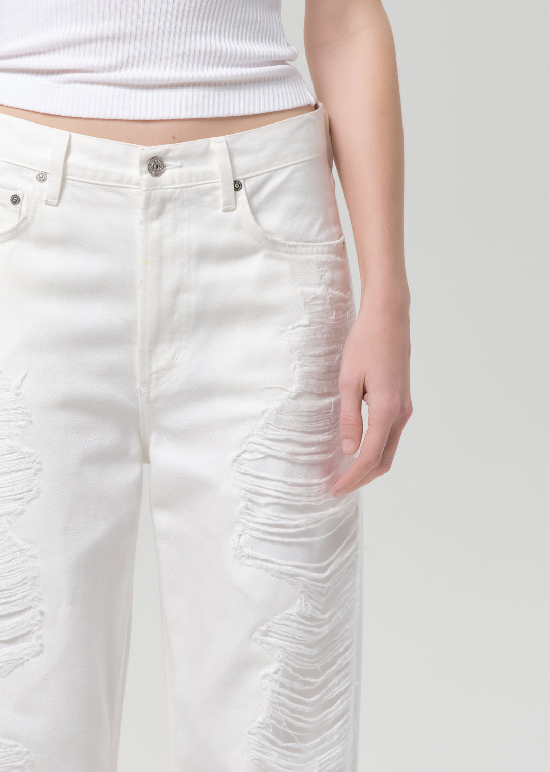 White distressed jeans worn by a person on a plain background