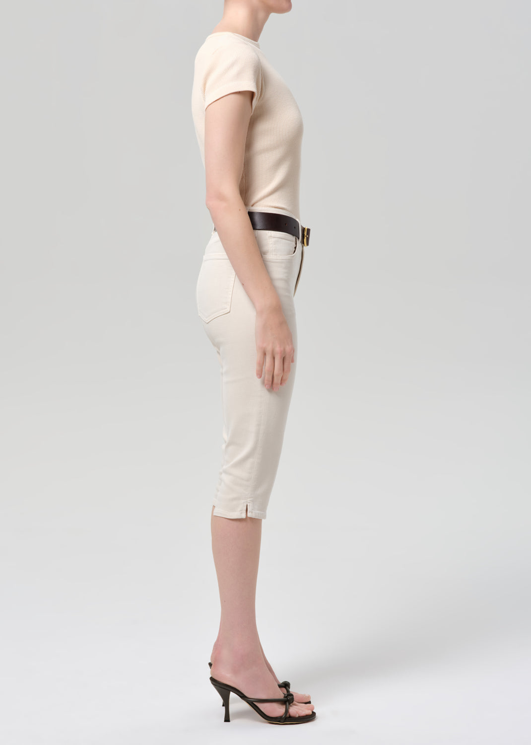 Person wearing a beige top and off-white pants with a belt on a light gray background