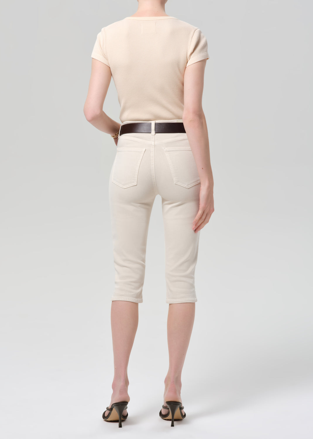 Person wearing a beige top and off-white pants with a belt on a light gray background