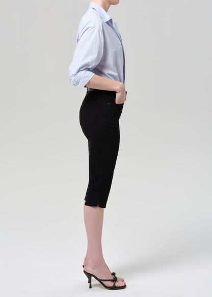 Person wearing a light blue shirt with rolled-up sleeves and black capris on a grey background