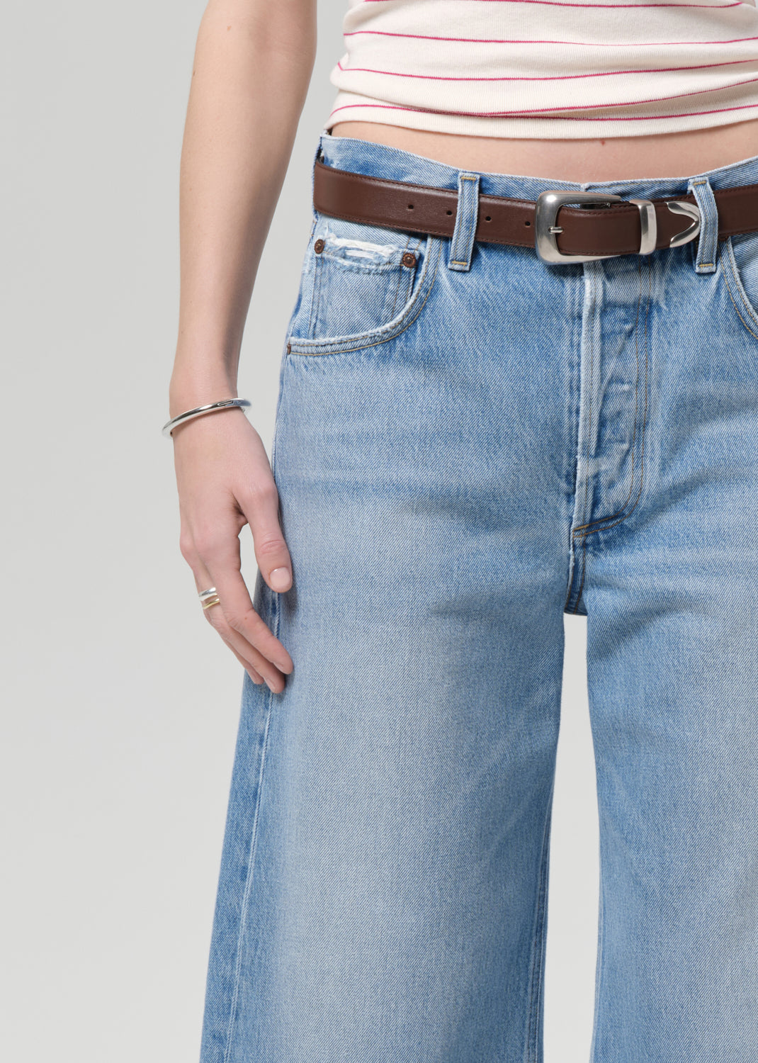 Person wearing light blue jeans with a brown belt on a plain background