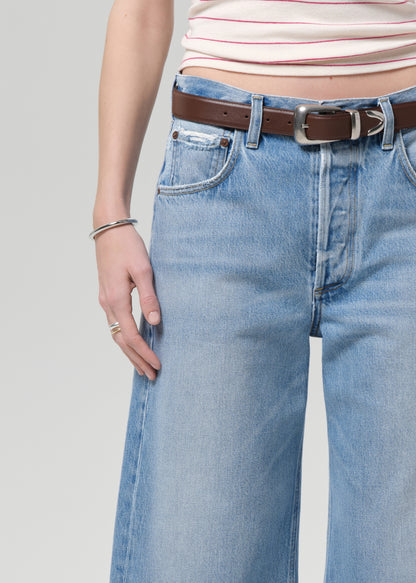 Person wearing light blue jeans with a brown belt on a plain background