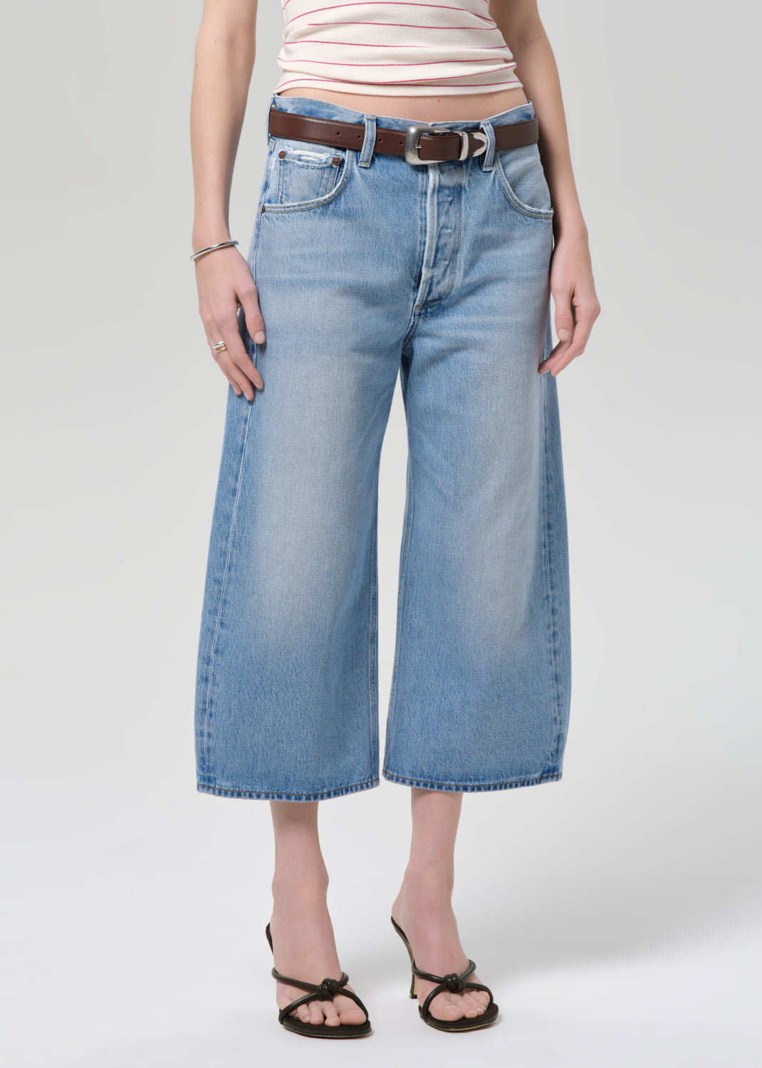 Person wearing blue jeans with a belt on a plain background