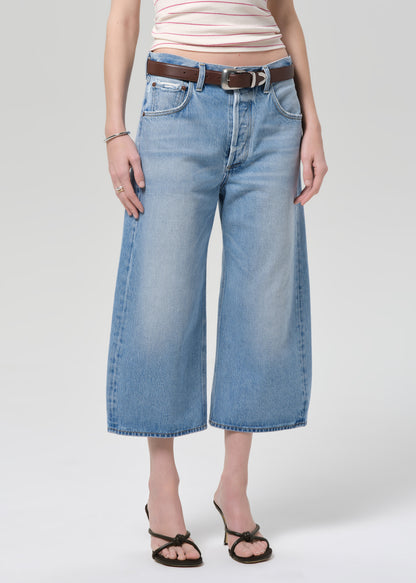 Person wearing blue jeans with a belt on a plain background