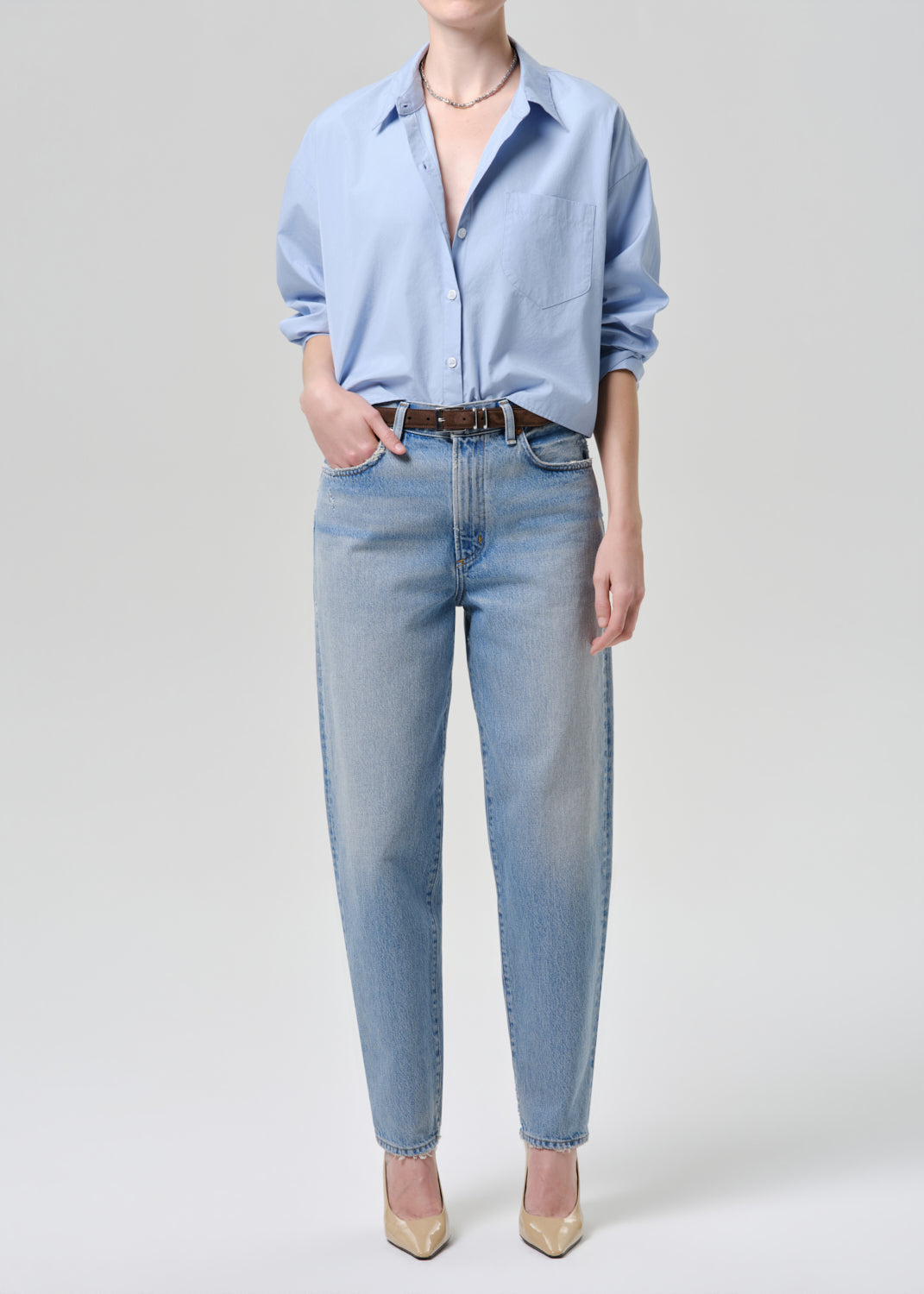 Person wearing a light blue shirt and jeans on a grey background