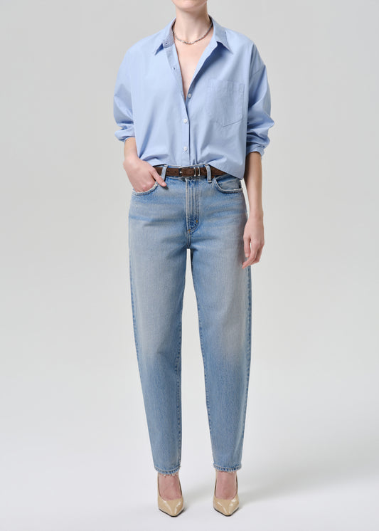 Person wearing a light blue shirt and jeans on a grey background