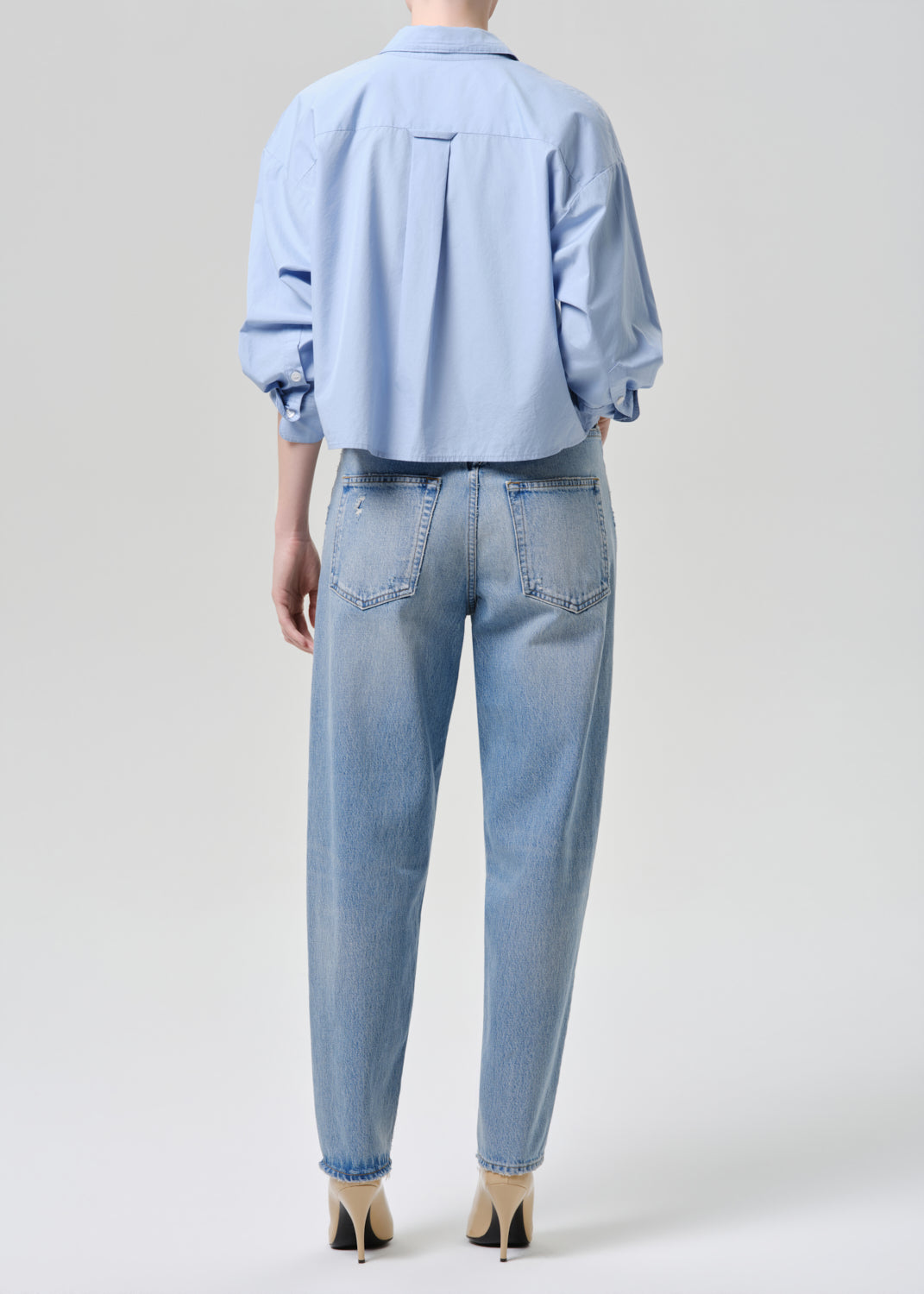 Person wearing a light blue shirt and jeans on a grey background