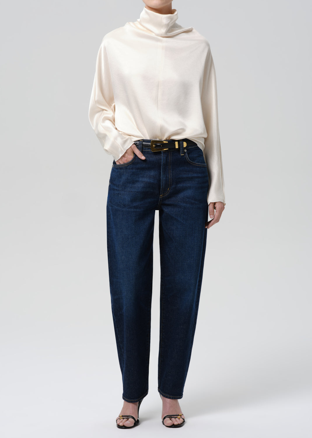 Person wearing a cream turtleneck and dark blue jeans on a grey background