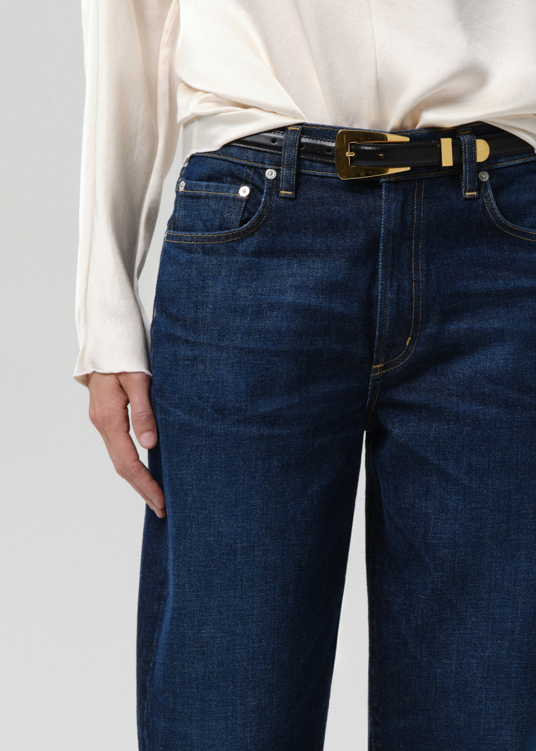 Person wearing blue jeans with a white shirt on a grey background