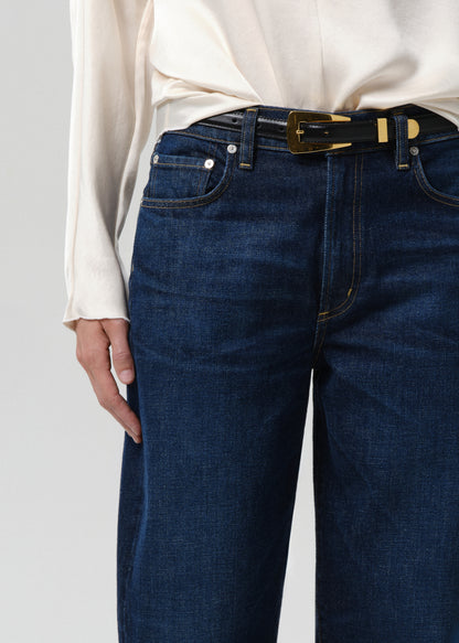 Person wearing blue jeans with a white shirt on a grey background