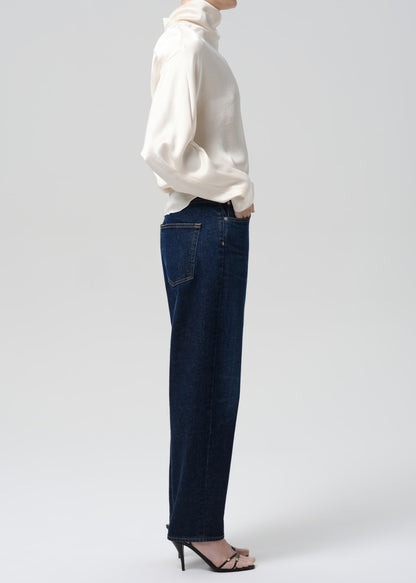 Person wearing a white turtleneck and dark blue jeans on a grey background