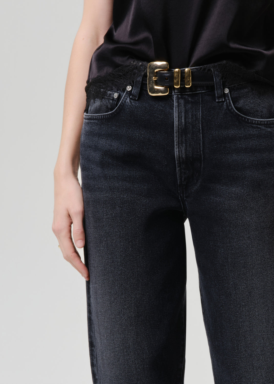 Person wearing black jeans with a gold belt on a grey background