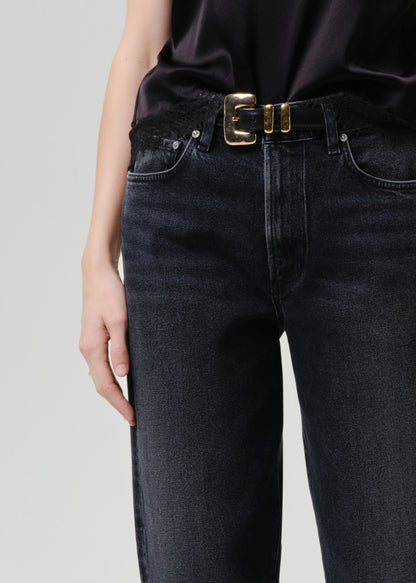 Person wearing black jeans with a gold belt on a grey background