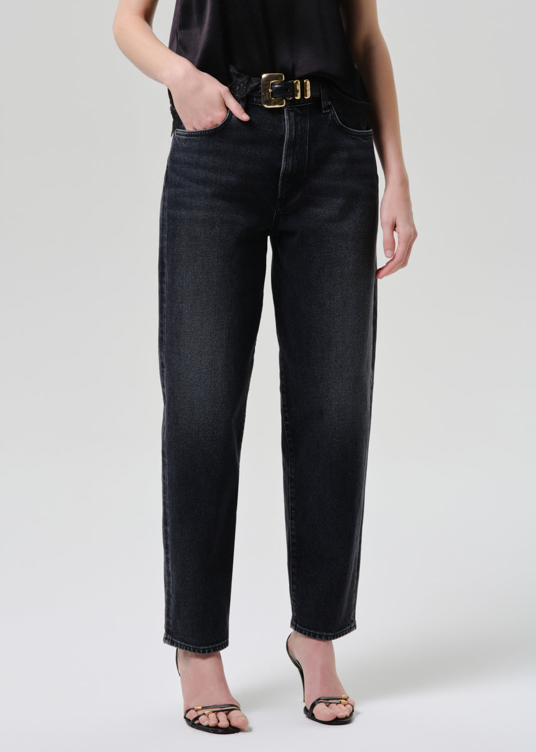 Person wearing black jeans with a gold belt on a grey background