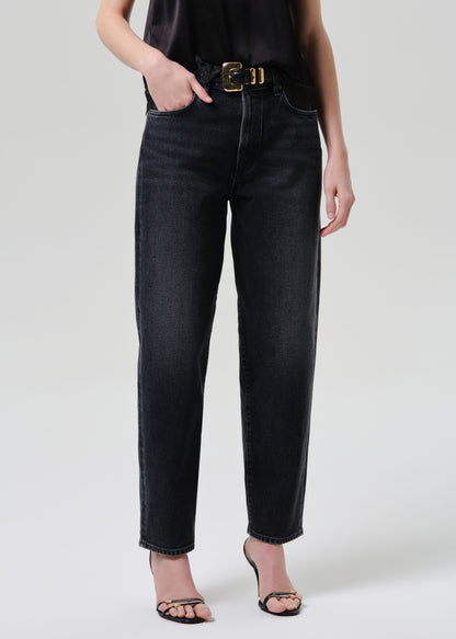 Person wearing black jeans with a gold belt on a grey background